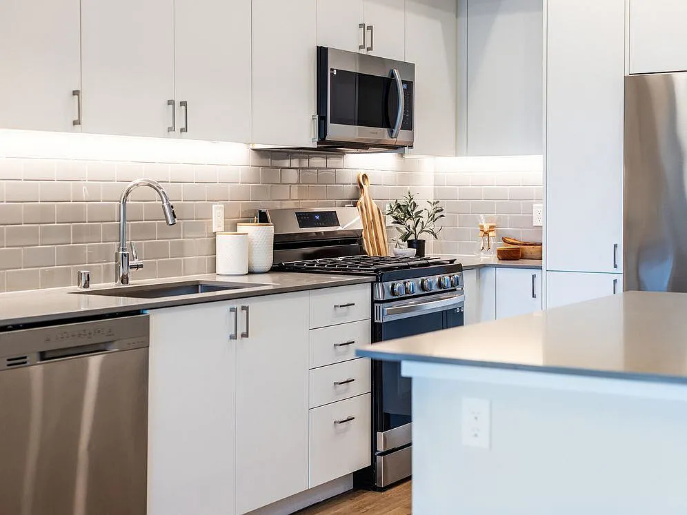 Kitchen with grey quartz countertops, white cabinetry, grey subway tile backsplash, stainless steel appliances, and hard surface flooring - Avalon Bothell Commons