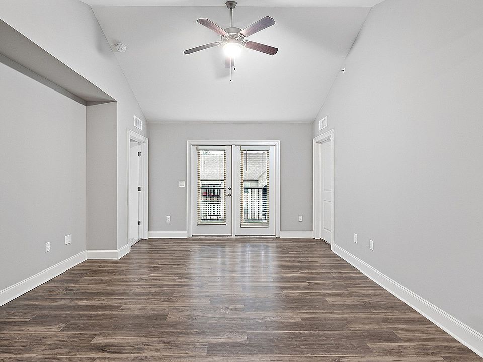 Bright and spacious living area with elegant wooden flooring, modern ceiling fan, and double doors leading to a balcony.