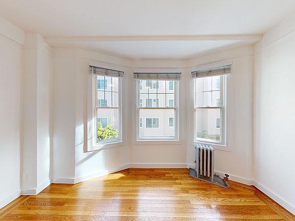 Bright, empty room with polished hardwood floors and a bay window.