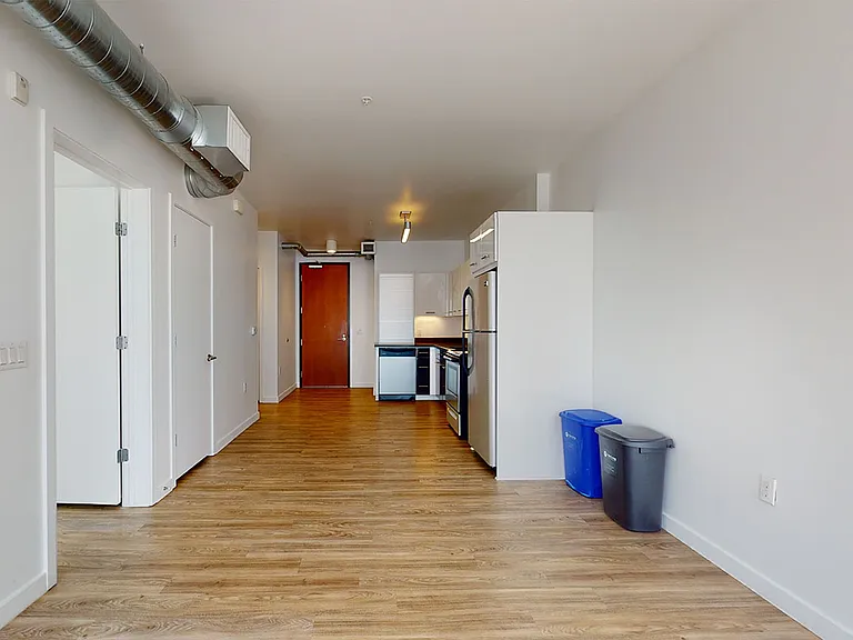 Apartment kitchen with stainless steel appliances, dining and living room with wood-style flooring.