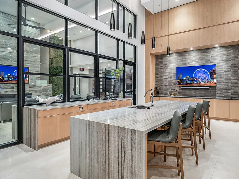 Modern kitchen with sleek marble island, stylish bar stools, and large windows offering natural light and views into a chic living area.