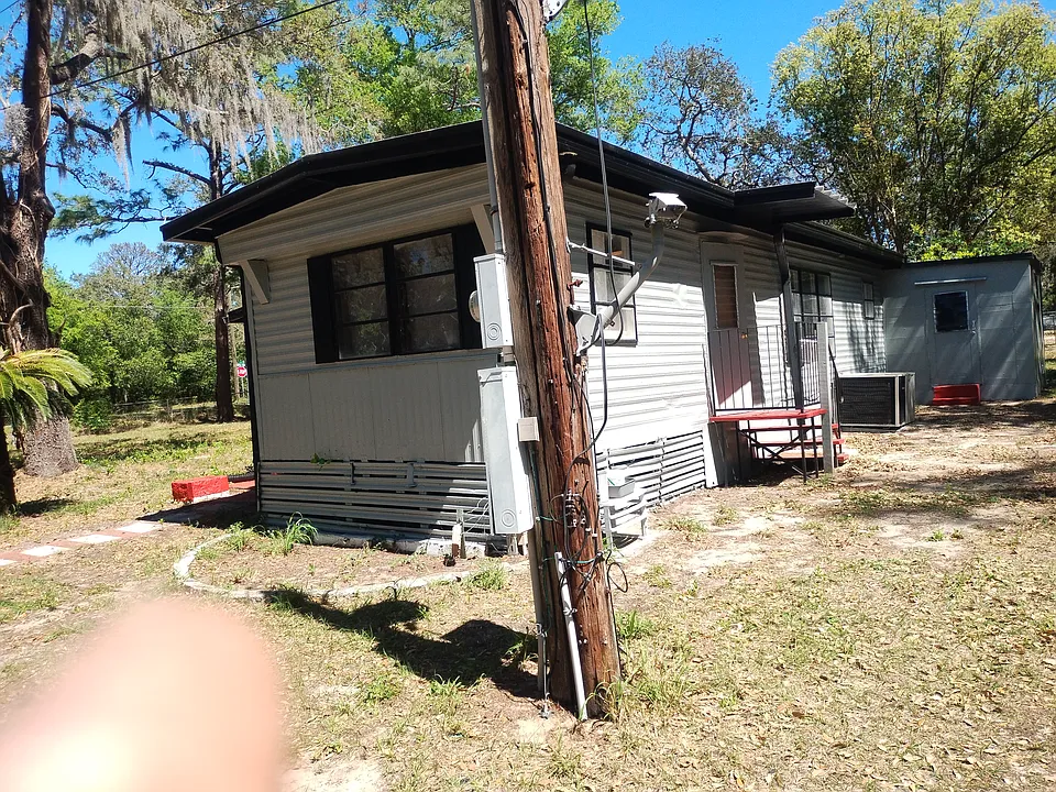 Photo of home, showing large kitchen to the left, steps and entry door, living room, bedrooms & large laundry room at the end of bldg. Laundry room has new ceiling, new concrete floor, 4-level metal shelf & exit/entry door w/steps. Washer & dryer inside.