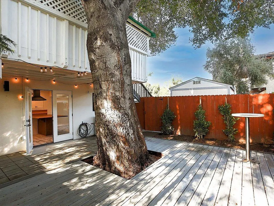 View of outdoor deck and patio area with newly planted hedge, which will grow to cover (and reach above) the fence