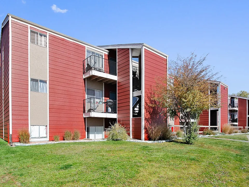 Charming red apartment complex with modern balconies set amidst lush green lawns and mature trees, capturing a serene suburban atmosphere.