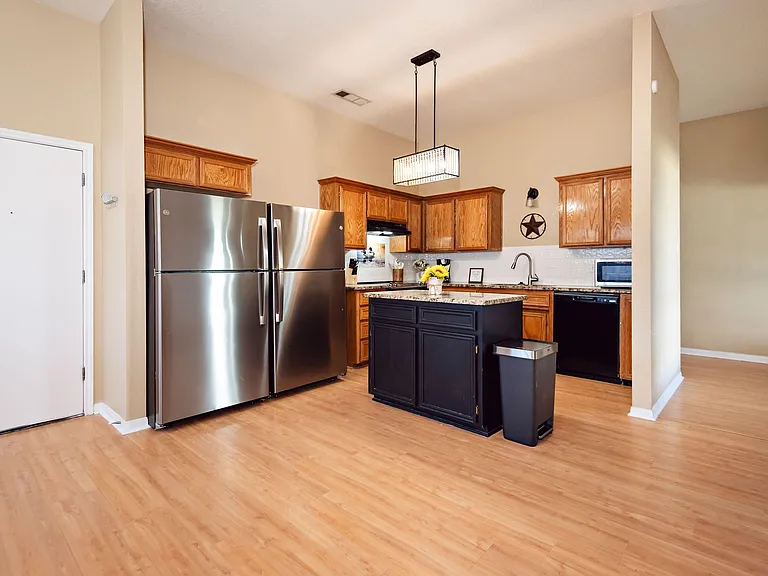 Open kitchen with island workspace, stainless refrigerator, ample cabinetry, and a sink with dishwasher for easy cleanup.