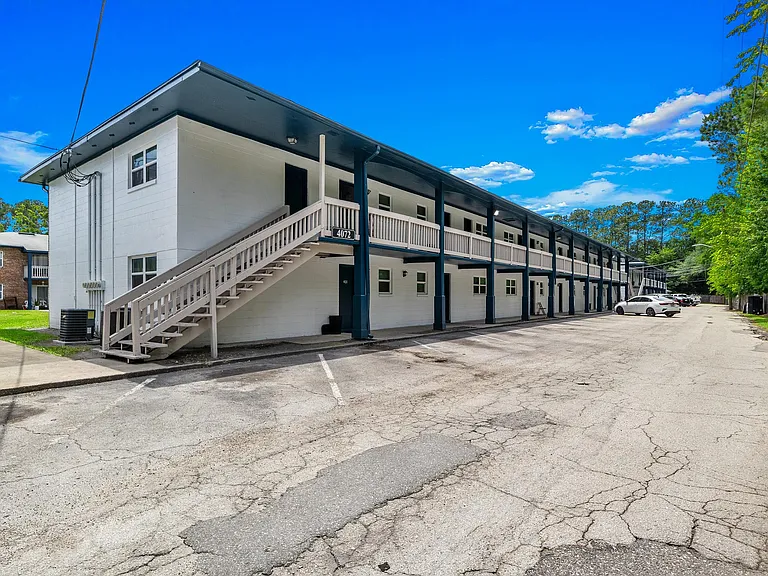Charming two-story apartment complex with modern exterior and ample parking, surrounded by lush greenery.