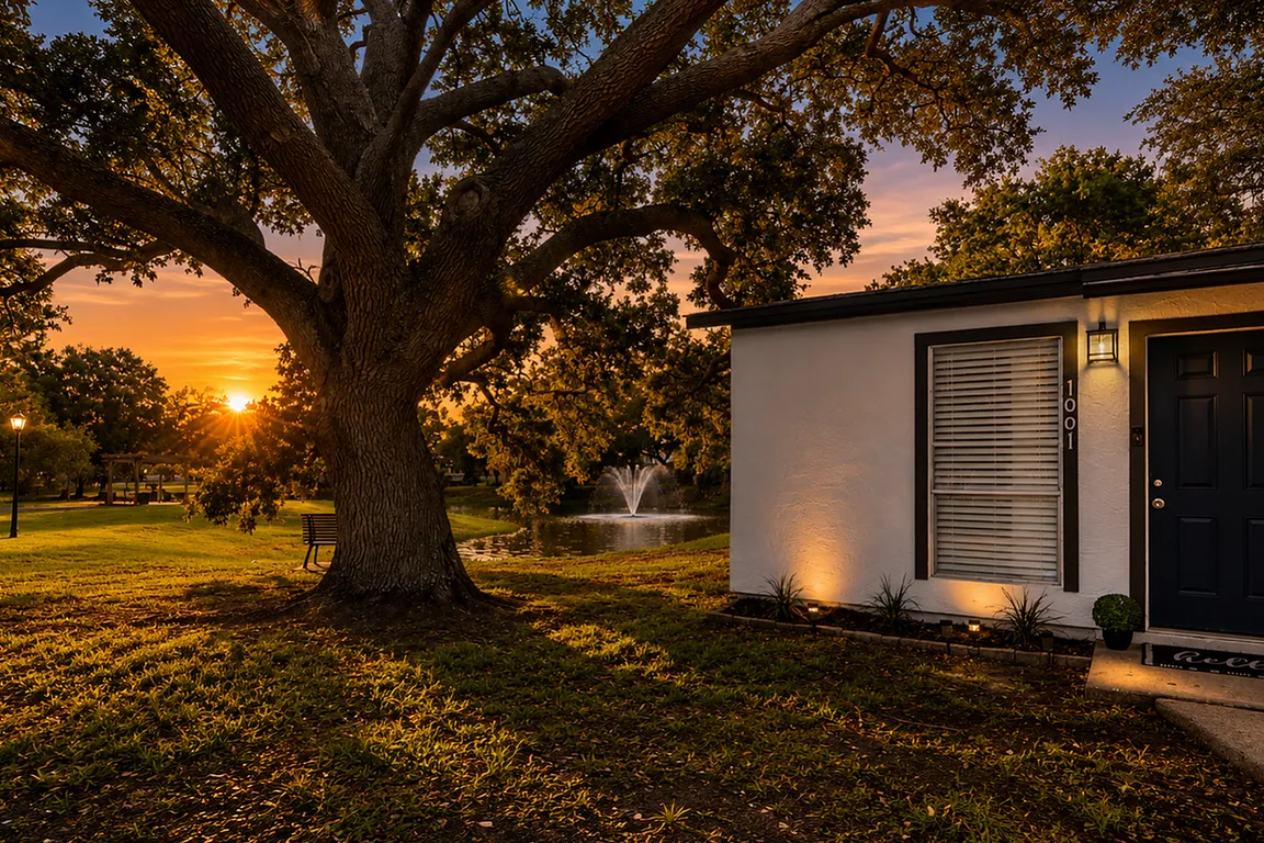 Charming home exterior bathed in sunset glow, featuring a lush lawn, majestic oak tree, and tranquil pond with fountain.