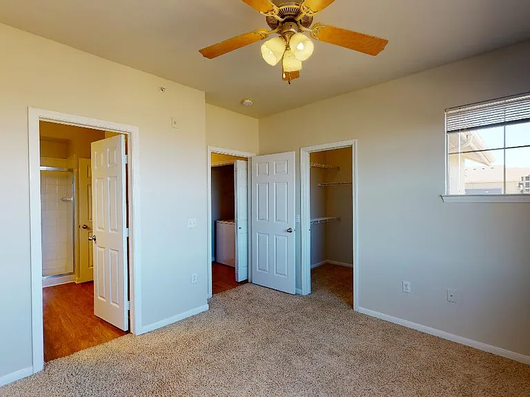 Spacious apartment bedroom with large closet, attached bathroom and plush carpet flooring.