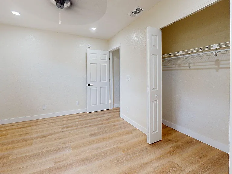 Inviting bedroom with elegant wood flooring, spacious closet, and modern ceiling fan for a comfortable living experience.