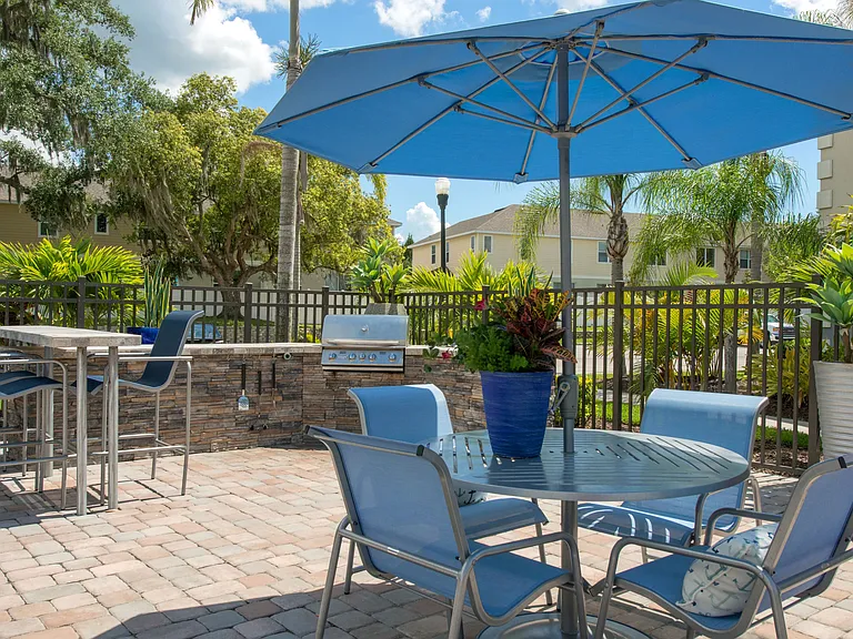 Enjoy outdoor dining at Soleil Blu Apartments in St Cloud, FL, featuring a modern outdoor kitchen with a gas grill, shaded seating, and beautiful landscaping, perfect for entertaining and relaxing.