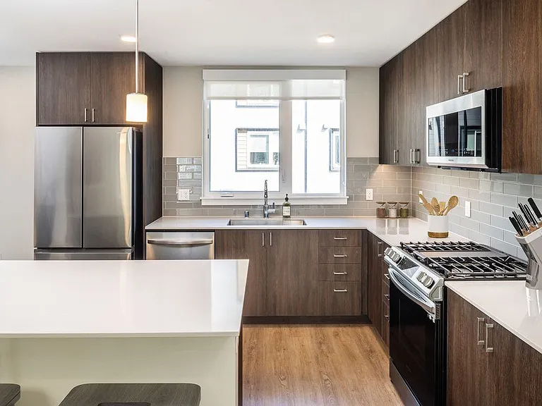 Townhome kitchen with white quartz countertops, dark cabinetry, grey subway tile backsplash, stainless steel appliances, and hard surface flooring