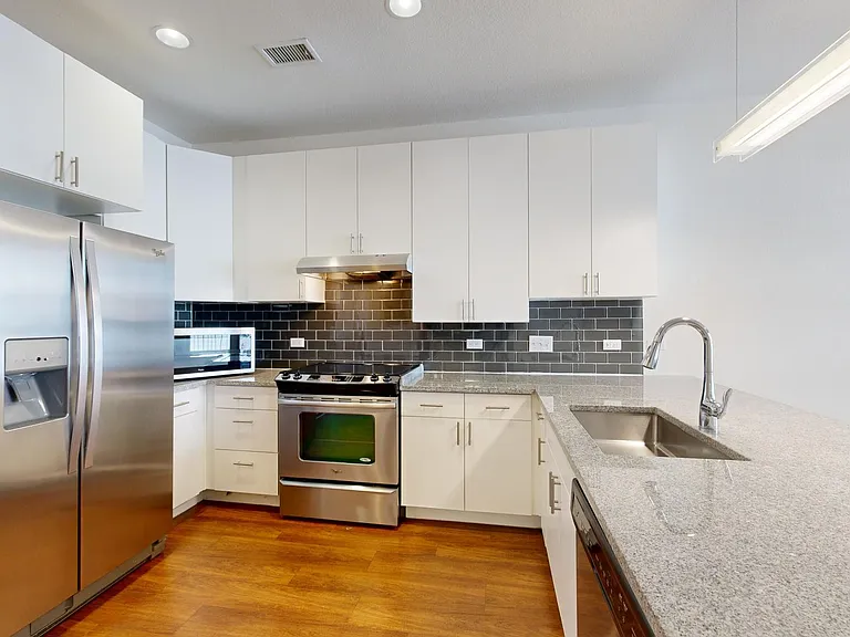 Apartment kitchen with stainless steel appliances, granite countertops, and wood-style flooring.