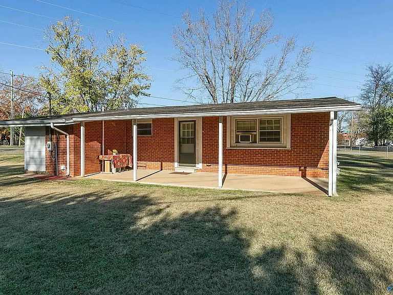 The covered back patio showing, from right to left, master bedroom window, back entrance which enters into the 3rd bedroom off the kitchen, kitchen window over sink, and the "L" where laundry room is inside the brick wall. Table shown is not available.