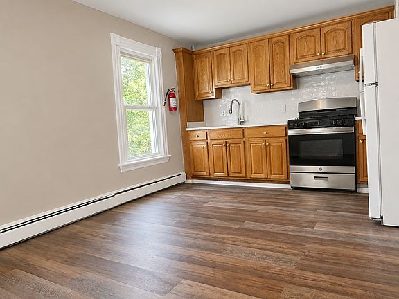 Spacious eat-in kitchen with newer flooring, stainless gas range, full-size refrigerator, classic wood cabinets, and room for a dining table.