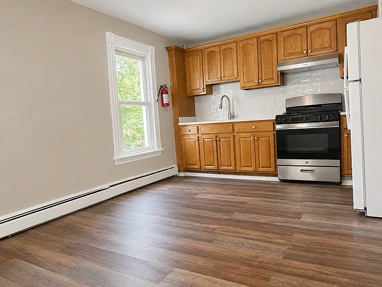Spacious eat-in kitchen with newer flooring, stainless gas range, full-size refrigerator, classic wood cabinets, and room for a dining table.