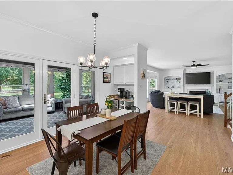 Dining area featuring a contemporary chandelier, wood-finish flooring, white trim, and double glass-paneled doors opening to an enclosed patio