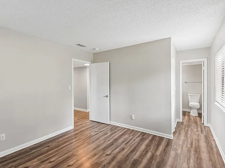 Bright, modern room with sleek wood flooring, neutral walls, and a cozy adjoining bathroom.