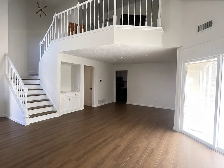 Living room, looking towards dining space, bar, and downstairs half bath. Upstairs Loft is visible from living room. Sliding glass door leads to private patio.
