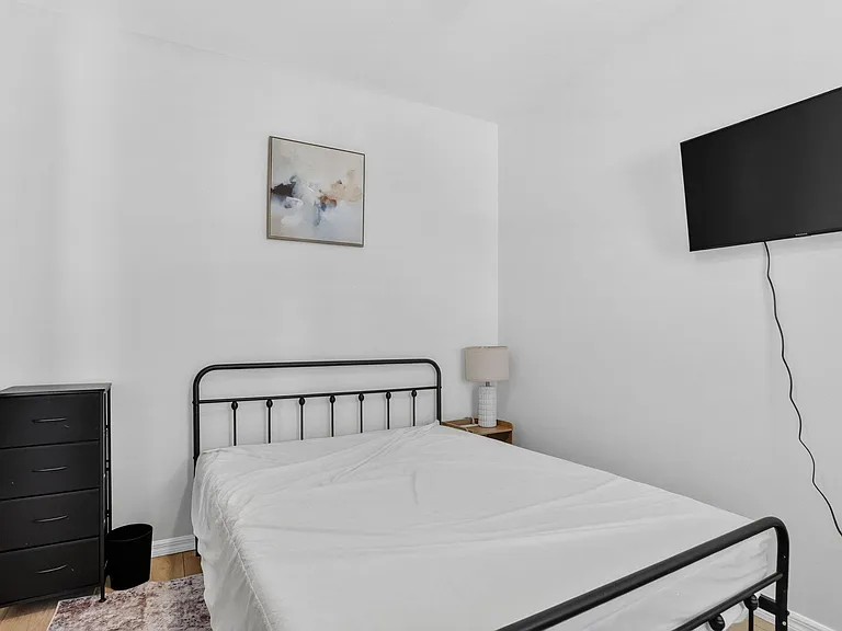 Private bedroom with a full bed, dresser storage, nightstand with lamp, and wall-mounted TV for easy entertainment.