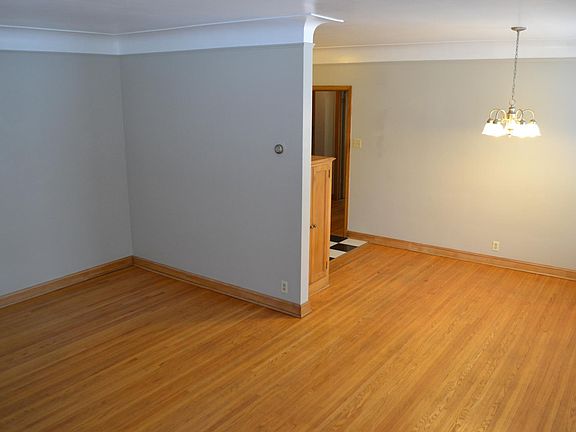 Large living room area with no furniture - the dining area is to the right and you can see the black/white kitchen floor tile (kitchen is behind the wall to the right