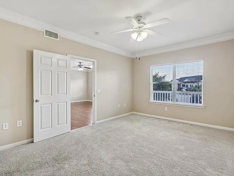 Bright and airy bedroom with plush carpeting, ceiling fan, and large window offering scenic views. Bright and airy bedroom with plush carpeting, ceiling fan, and large window offering scenic views.
