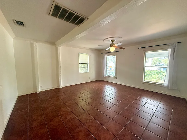 View of primary bedroom from doorway - front windows look out onto porch and yard with side window into shaded, small side yard.