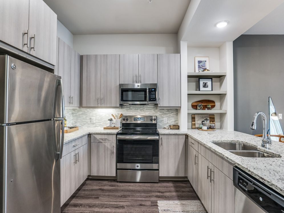 Gray finish package kitchen with speckled granite countertop, stainless steel appliances, and hard surface flooring.