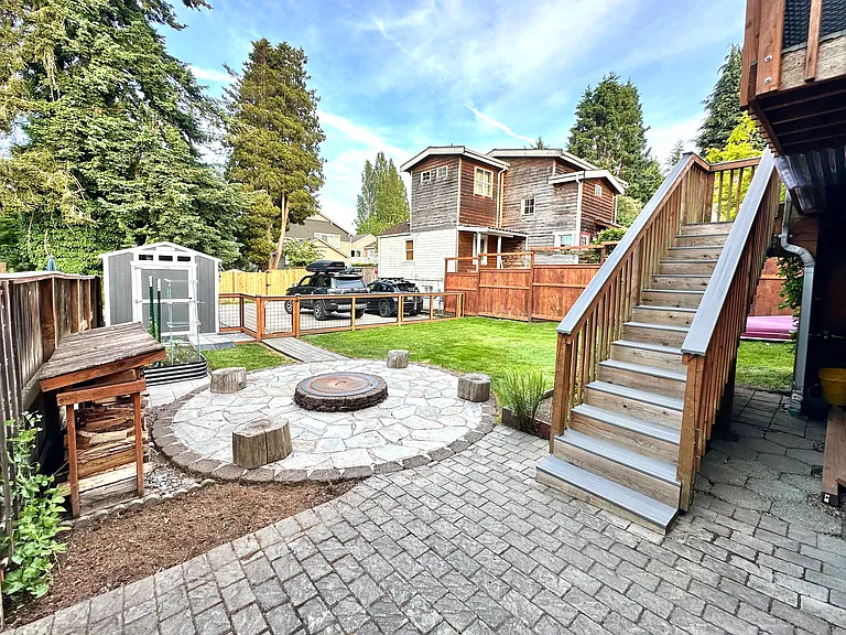 View of back yard and parking spot with two small garden beds for tenant and shared fire pit.