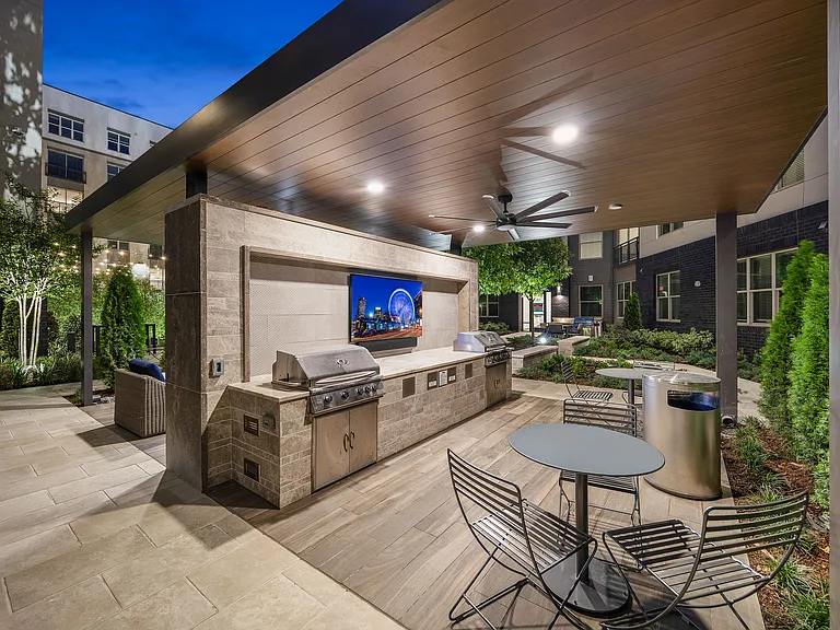 Luxurious outdoor kitchen with high-end grills, cozy seating, and modern lighting in a beautifully landscaped apartment courtyard.