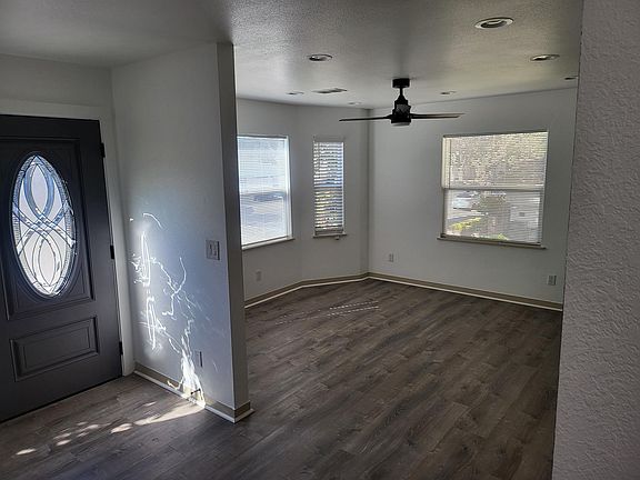 Front entrance and living room space with new ceiling fans, blinds, wood look laminate floors and freshly painted.