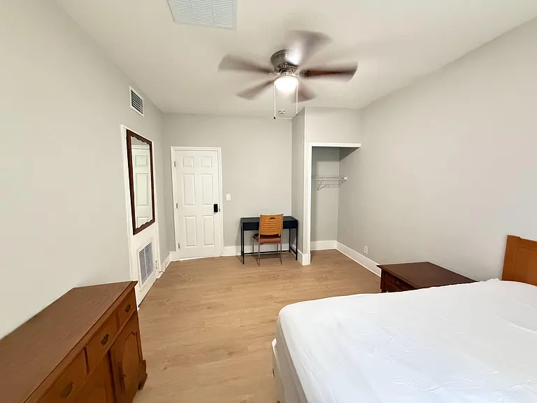 Spacious bedroom with ceiling fan, wood-look flooring, open closet storage, and a dedicated desk area for work or study.