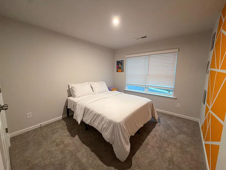 Comfortable bedroom with carpeted flooring, a full bed setup, and a large window with blinds for light and privacy.