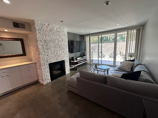 Open living room with bar/cabinets, custom stone fireplace (gas, operated with a switch), and large sliding glass doors to the patio