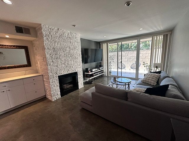 Open living room with bar/cabinets, custom stone fireplace (gas, operated with a switch), and large sliding glass doors to the patio