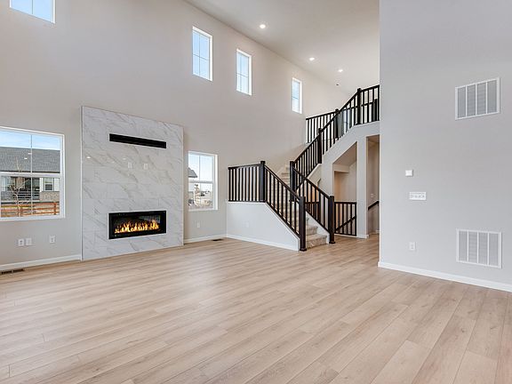 A spacious and bright living room with a fireplace, wooden floors, and a staircase leading to an upp