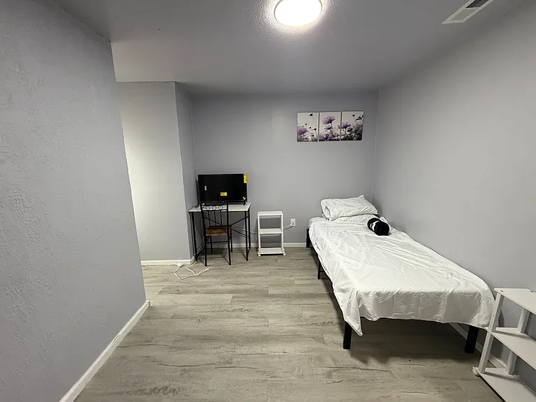Furnished bedroom with twin bed, TV, and compact desk area, plus durable flooring and neutral finishes.