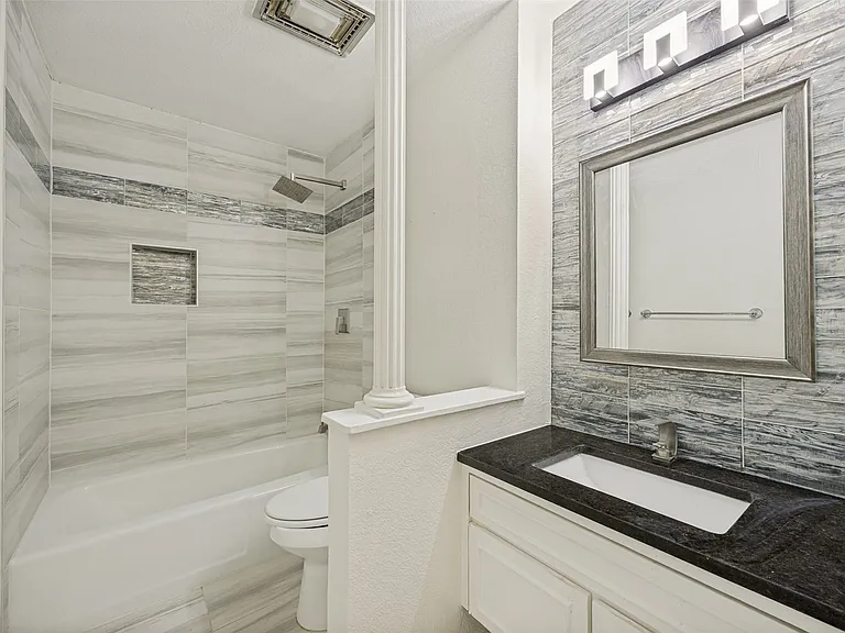 Bathroom featuring a vanity with a dark countertop and integrated sink, a large framed mirror, and a modern light fixture
