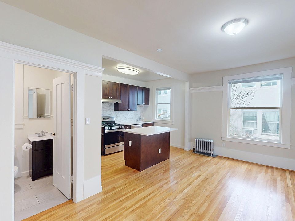 Living room with hardwood floor, open-plan kitchen, dark wood cabinetry, and adjacent bathroom