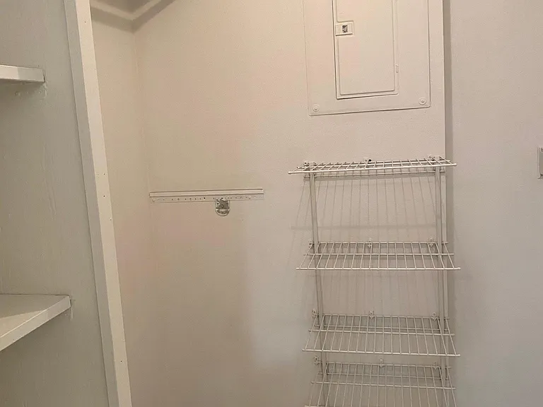Multiple white wire shelves and hanging rod for long dresses. At center is electrical panel.