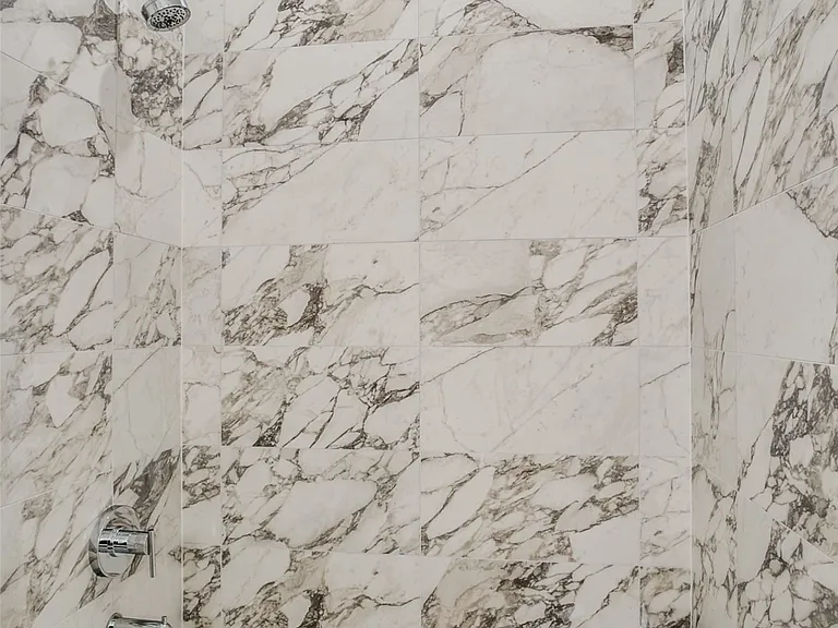 Bathtub with floor-to-ceiling marbled tile surround and chrome fixtures