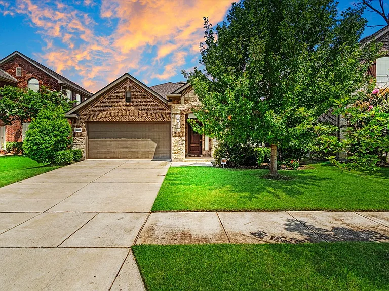 Brick and stone facade residence featuring an attached garage, a concrete driveway, and a well-maintained lawn with established trees