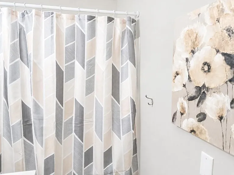 Bathroom tub/shower area with a patterned shower curtain and wall art for a clean, finished look.