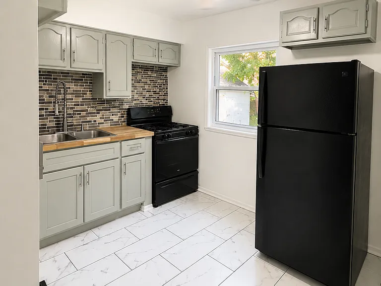 Bright updated kitchen featuring modern cabinetry, tile flooring, backsplash, and black & stainless steel appliances.