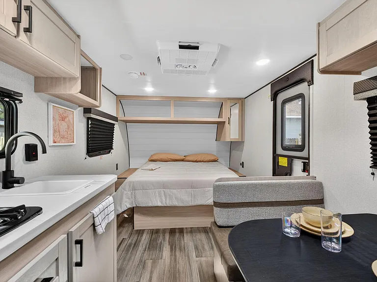 Compact studio-style sleeping area with built-in cabinetry, kitchenette, and dinette, plus windows with blinds for privacy.