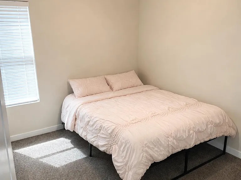 Private bedroom with a full bed, neutral walls, carpeted flooring, and ceiling fan lighting plus a window with blinds.