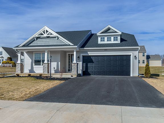 Angled front exterior showing gabled rooflines, covered porch with stone columns, and attached two-c
