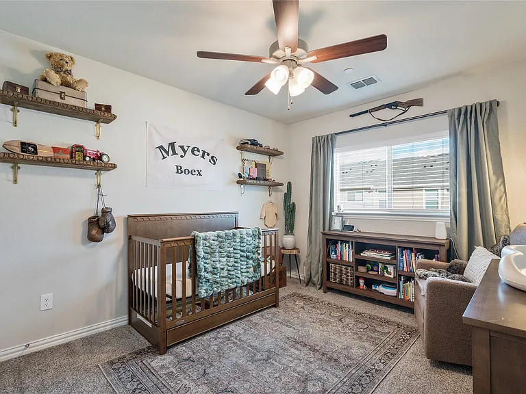Carpeted room featuring a ceiling fan with light fixture, built-in shelving, window with blinds and drapery, and a decorative area rug