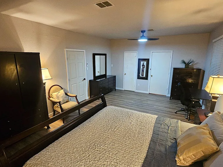 Spacious furnished bedroom with hardwood-style floors, ample storage, a work desk, and ceiling fan for comfort.