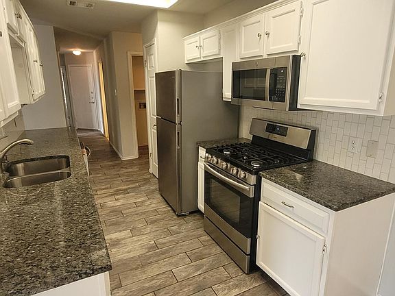 Modern kitchen featuring granite countertops, stainless steel appliances, and white cabinetry. Includes a gas stove, microwave, and spacious refrigerator. Elegant tile flooring and ample storage space create a functional and stylish cooking area.