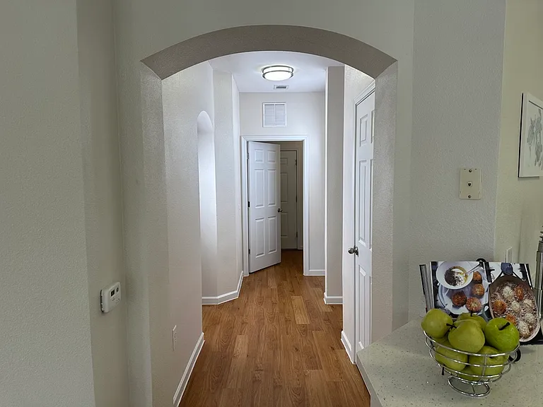 Bright hallway with elegant archway and warm wooden composite flooring, leading to white panel doors, accentuating a welcoming home ambiance. Bright hallway with elegant archway and warm wooden composite flooring, leading to white panel doors, accentuatin